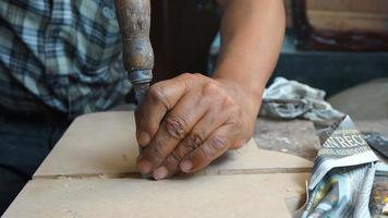 Die Hand des Zimmermanns hält einen Meißel, der ein Holzbrett auf seinem Schreibtisch modelliert foto