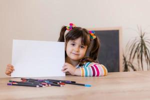 ein süßes kleines mädchen in einer zeichenstunde hält ein leeres weißes blatt in den händen, ein platz für text. Kinder und Kreativität. hochwertiges Foto