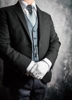 Porträt eines Butlers oder Hotelportiers in dunklem Anzug und weißen Handschuhen, die begierig darauf sind, Ihnen behilflich zu sein. Konzept eleganter Gastfreundschaft und professioneller Höflichkeit. foto