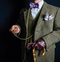 Porträt eines britischen Herrn in Tweed-Anzug und Lederhandschuhen mit goldener Taschenuhr auf schwarzem Hintergrund. Retro-Stil und Vintage-Mode. foto