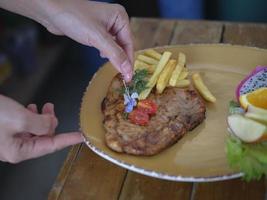 Die Hand des Küchenchefs bereitet gegrillte Schweinerippchen zu und dekoriert Blumen. foto