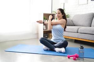 asiatische frau, die ihre schultern in yoga und übung zu hause während covid-19 streckt. foto