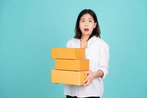 junge schöne asiatische Geschäftsfrau in weißer Freizeitkleidung, die isoliert auf hellgrünem Hintergrund steht. sie ist schockiert und hält paket paketkasten. foto