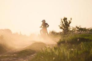 Foto eines Motorradfahrers bei Sonnenuntergang, der mit Geschwindigkeit die Straße entlang fährt