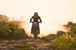 Foto eines Motorradfahrers bei Sonnenuntergang, der mit Geschwindigkeit die Straße entlang fährt