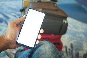 Smartphone mit leerem Bildschirm und Kofferstapel am Flughafen halten foto