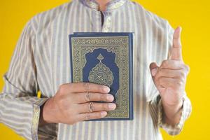 muslimischer Mann, der den Koran des Heiligen Buches mit Kopienraum hält foto