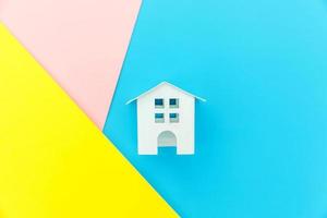 einfach design mit miniatur-weißem spielzeughaus isoliert auf blau gelb rosa pastell bunt trendy geometrischen hintergrund hypotheken-sachversicherung traumhaus konzept. flach liegend draufsicht kopierraum. foto