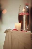 Hochzeitsdekoration eine Kerze und eine Vase mit Wasser auf einem weißen Tisch. Flaschen mit Wasser und eine schwimmende Kerze foto