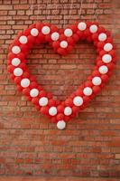 Herz aus Luftballons vor dem Hintergrund der Wand. Konzept für den Valentinstag. das design der luftballons ist weiß-rot mit einem großen herz in der mitte. Bandagiertes festliches Band. foto