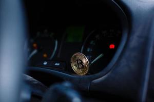 Gold-Bitcoin auf dem Armaturenbrett des Autos neben dem Kraftstoffverbrauch foto