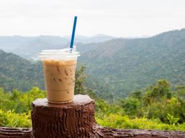 Ein Glas Eiskaffee wird vor dem Hintergrund von Bergen und Himmel auf den Zaun gestellt. foto