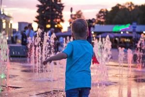 Kinder haben Spaß daran, sich im Sonnenuntergang in den Springbrunnen in der Nähe des Gebäudes im Park zu vergnügen. Abendspaziergang durch die Stadt. foto