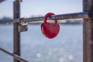 Am Zaun der Brücke hängt ein herzförmiges Türschloss, ein Symbol für Liebe und Treue mit einem See im Hintergrund. Das herzförmige Schloss symbolisiert Treue und Liebe foto