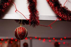 glänzender weihnachtsroter Ball, der an Tannenzweigen mit festlichem Hintergrund hängt foto
