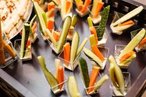 Catering für Partys. nahaufnahme von vorspeisen mit kirschtomaten, grünen oliven, olivenöl, käse und gewürzen in kurzen gläsern auf holzbraunem tisch. foto