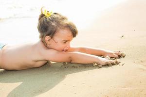 glückliches kleines Mädchen, das auf dem Sand am Strand liegt foto