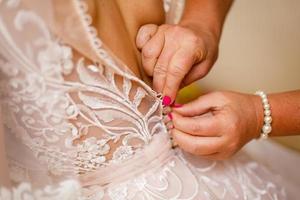 Die Hand der Freundin umklammert Knöpfe am Korsett der Braut foto