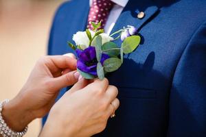 Nahaufnahme der Hände der Braut, die Ansteckblume an der Jacke des Bräutigams feststecken foto