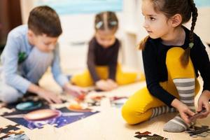 Kinder verbinden Puzzleteile in einem Kinderzimmer im Erdgeschoss zu Hause. lustige familienaktivität freizeit. foto