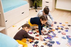 Kinder verbinden Puzzleteile in einem Kinderzimmer im Erdgeschoss zu Hause. lustige familienaktivität freizeit. foto