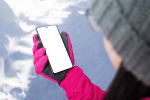 mädchen mit hut, jacke und handschuhen hält ein handy mit einem isolierten bildschirm foto