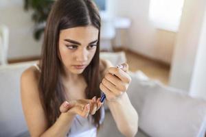 Frau mit Lanzette am Finger. Frau macht Blutzuckertest zu Hause in einem Wohnzimmer. Diabeteskontrolle foto