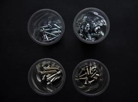 Baubolzen und Schrauben in Plastikbechern auf schwarzem Hintergrund. Bauzubehör. foto