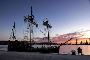 Silhouettenfoto eines im Hafen festgemachten Segelschiffs und eines Fischers am Abend foto