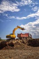 Gelber Bagger und leerer Muldenkipper, der auf der Baustelle arbeitet. vertikale Ansicht foto