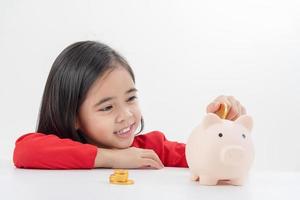 kleines asiatisches mädchen, das geld in einem sparschwein spart, über sparen lernt, kind spart geld für zukünftige bildung. geld, finanzen, versicherungen und personenkonzept foto