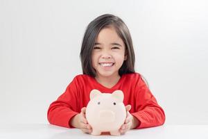 kleines asiatisches mädchen, das geld in einem sparschwein spart, über sparen lernt, kind spart geld für zukünftige bildung. geld, finanzen, versicherungen und personenkonzept foto