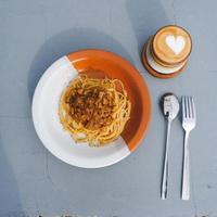 Gesunder Teller mit italienischen Spaghetti, gekrönt mit einer leckeren Bolognese-Sauce aus Tomaten und Rinderhackfleisch und frischem Basilikum auf einem grauen Tisch. mit Cappuccino serviert foto