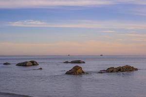 schöner felsenstrand sonnenaufgang frische meeresbrise sommerferien. goldener und blauer himmel mit weißen wolken. foto