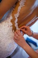 Braut, die ihr weißes Hochzeitskleid anzieht foto