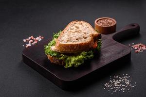 Frisches, leckeres Sandwich mit Hähnchen, Tomaten und Salat auf einem schwarzen Teller foto