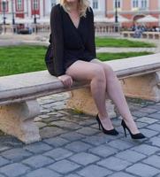Schönes blondes Modell, das ein kurzes schwarzes Kleid und High Heels trägt, hat ein Fotoshooting auf der Straße foto