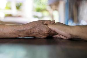 Nahaufnahme von zwei faltigen Händen zweier älterer thailändischer Frauen, die sich tröstend halten. foto