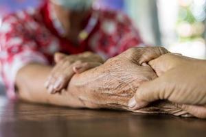 Nahaufnahme der Hände zweier älterer thailändischer Frauen, die sitzen und sich an den Händen halten. foto