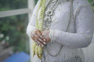 schöne braut, die ihre hand hält, während sie hochzeitskleid mit jasmin- und magnolienblumenhalskette für eine traditionelle hochzeitszeremonie in indonesien trägt foto