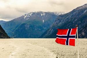 norwegische nationalflagge weht im wind im sognefjord mit bergen im hintergrund, aurlan, grafschaft sogn og fjordane, norwegen