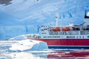 rotes kreuzfahrtpassagierschiff, das zwischen den eisbergen mit gletscherplatte im hintergrund treibt, neco bay, antarktis foto