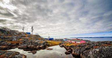 graue wolken, moosbewachsene felsen, see, wohnhäuser und funkturm im hintergrund in einem vorort von nuuk city, grönland foto