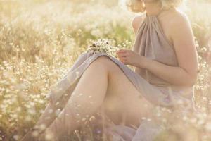 Nahaufnahme der jungen Frau mit Blumenstrauß, die auf dem Konzeptfoto der Wildblumenwiese sitzt foto