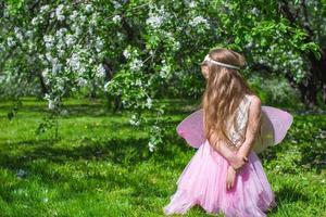 kleines süßes Mädchen mit Schmetterlingsflügeln im blühenden Apfelgarten foto