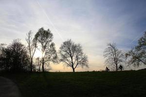 silhouette von leuten, die mit dem fahrrad auf einer landstraße bei sonnenuntergang entlang der donau in regensburg, deutschland, europa fahren. foto