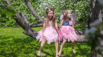 Kleine entzückende Mädchen mit Schmetterlingsflügeln auf blühendem Apfelbaum foto