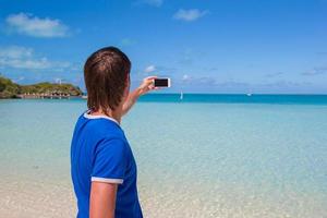 junger Mann in Weihnachtsmütze mit Telefon am tropischen karibischen Strand foto