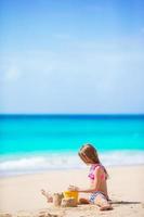 Entzückendes kleines Mädchen, das mit Strandspielzeug am weißen tropischen Strand spielt foto