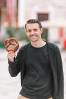 schöner junger Mann, der Brezel hält und sich im Park entspannt foto